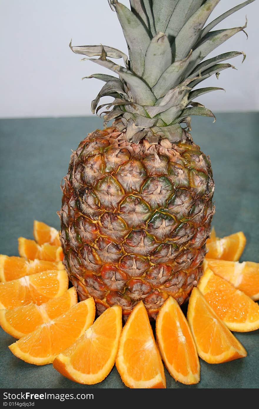 A pineapple with orange slices surrounding it on a green counter. A pineapple with orange slices surrounding it on a green counter.