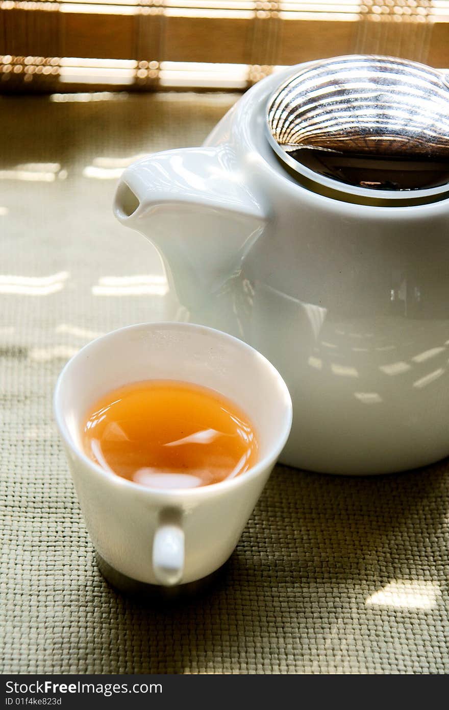 A picture of a cup of tea and a teapot basking under the sun. A picture of a cup of tea and a teapot basking under the sun