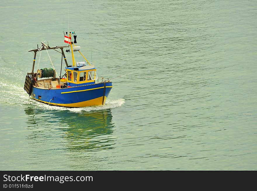A small fishing boat coming into harbour. Space for text on the water.