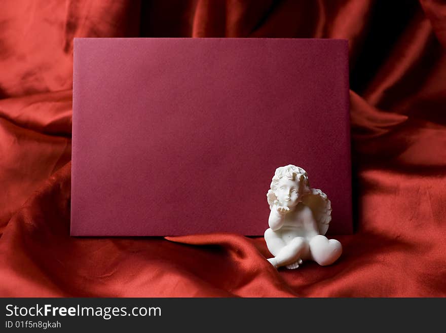 A red valentine card - letter on red satin fabric background with a little white angel sending a kiss to the message recipient.