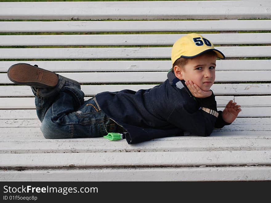 Young boy sitting on a bench in a park. Young boy sitting on a bench in a park.