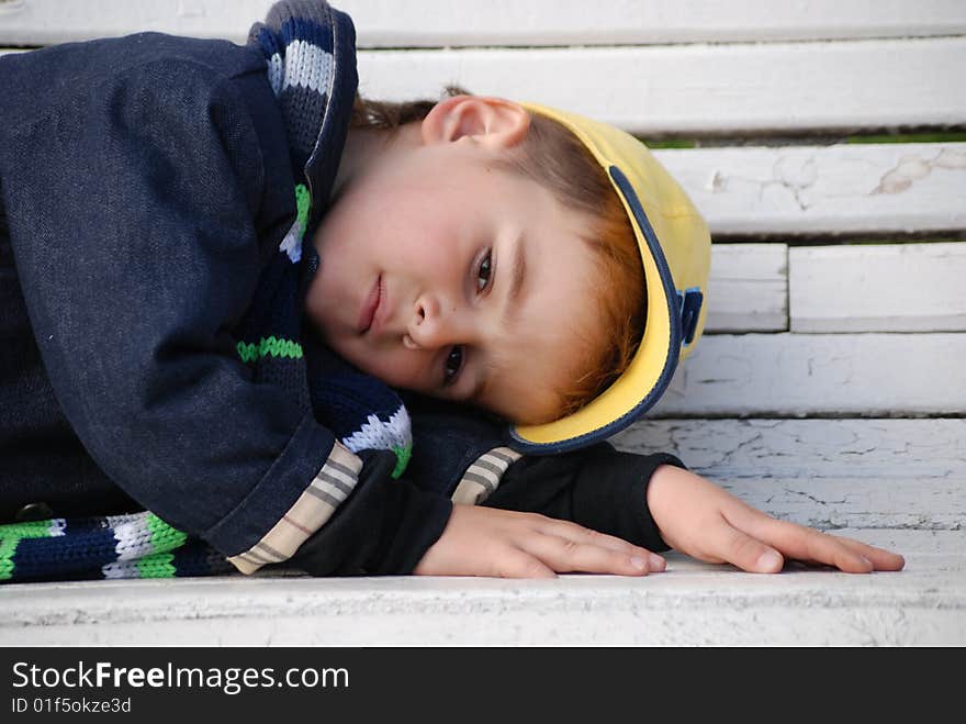 Young boy sitting on a bench in a park. Young boy sitting on a bench in a park.