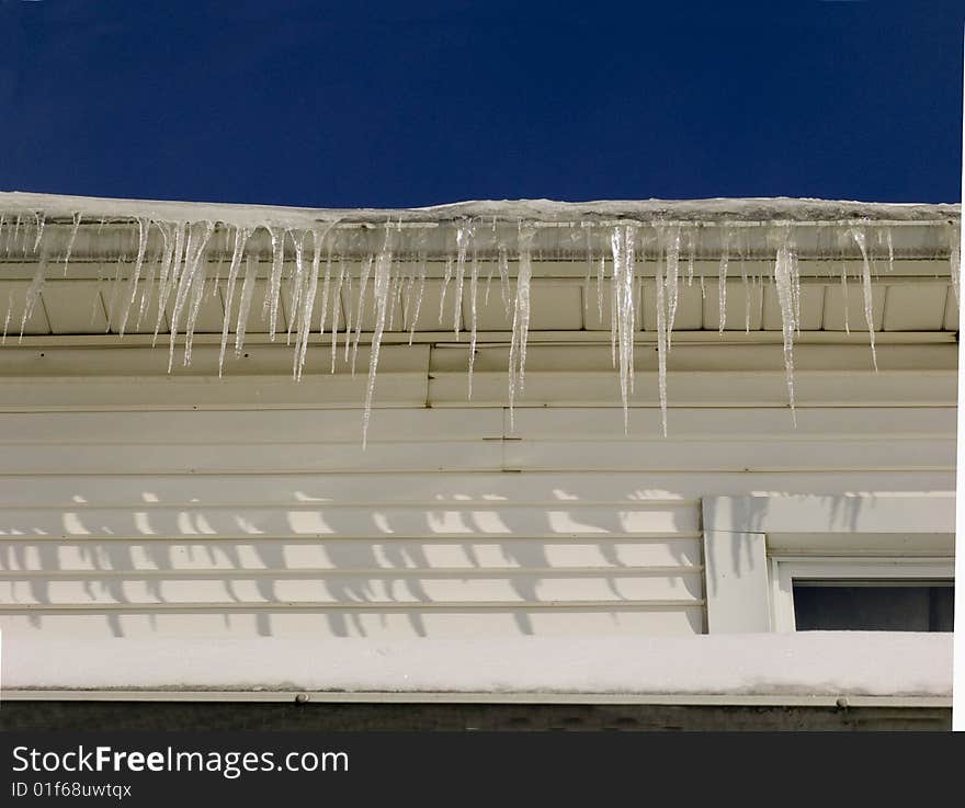 A row of icicles in a garage roof against a deep blue sky.