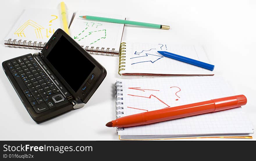 Open palmtop opposite four notebooks with felt-tip pens, crayon and wax pencil