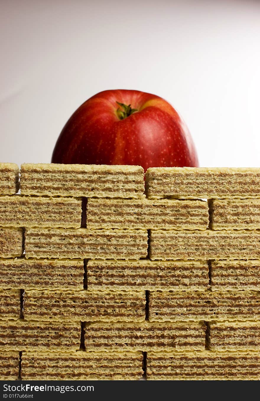 Diet difficulties - a healthy red apple behind a wall of unhealthy chocolate wafers - relation between healthy and junk food, fighting with addiction.