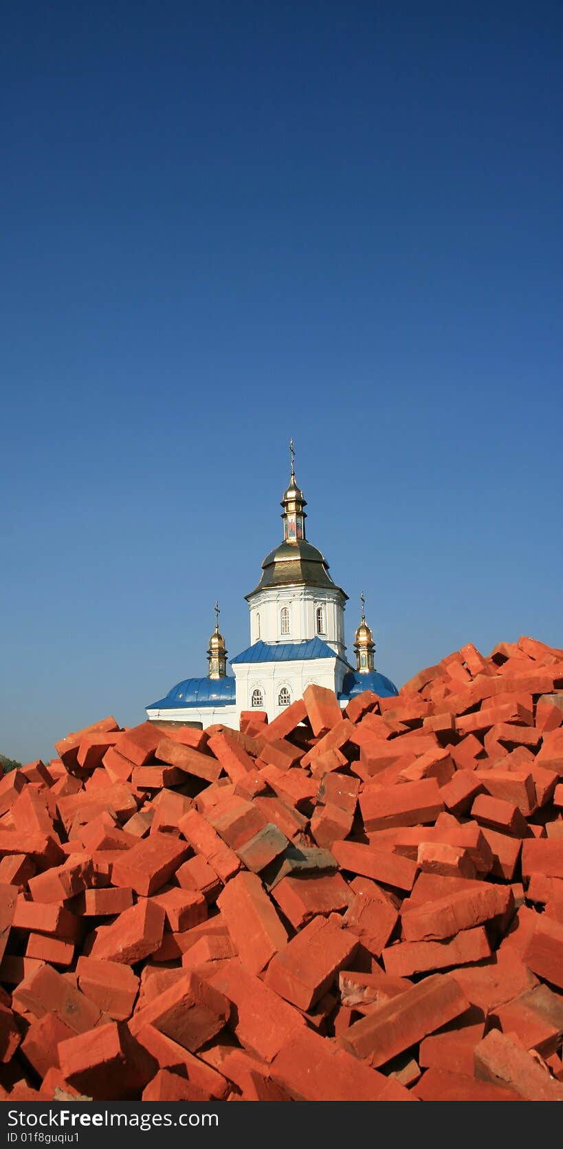 Renewed orthodox church over red bricks pile against deep blue sky. Renewed orthodox church over red bricks pile against deep blue sky