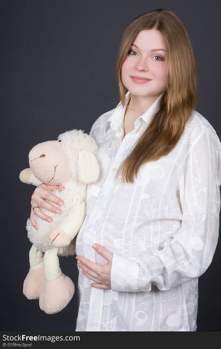 Beautiful pregnant woman in white holding toy on grey background. Beautiful pregnant woman in white holding toy on grey background