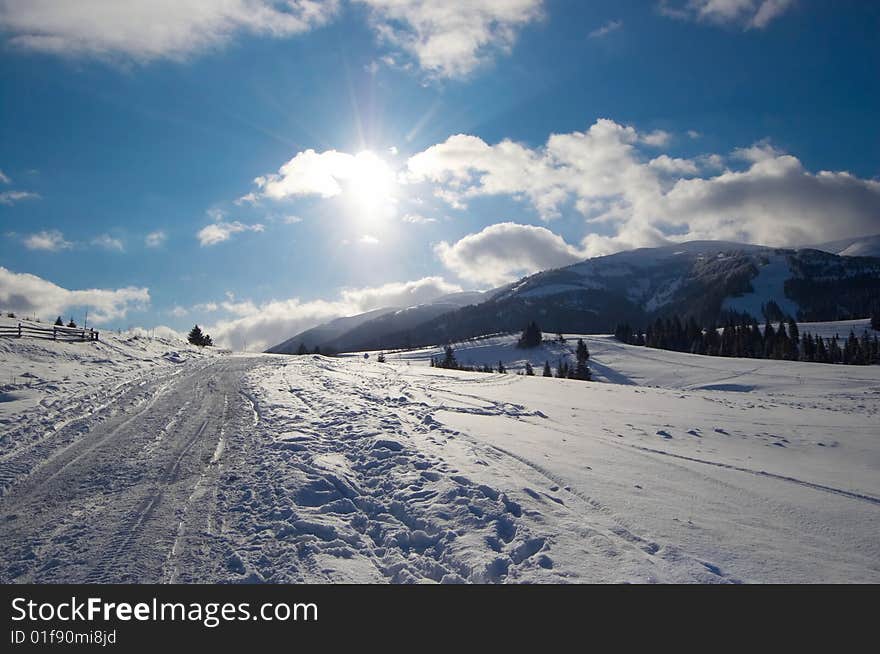 Winter mountains with bright sun on cloudy sky