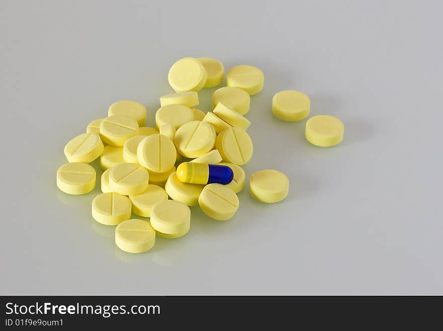 Pile of yellow pills and one blue and yellow capsule. Pile of yellow pills and one blue and yellow capsule