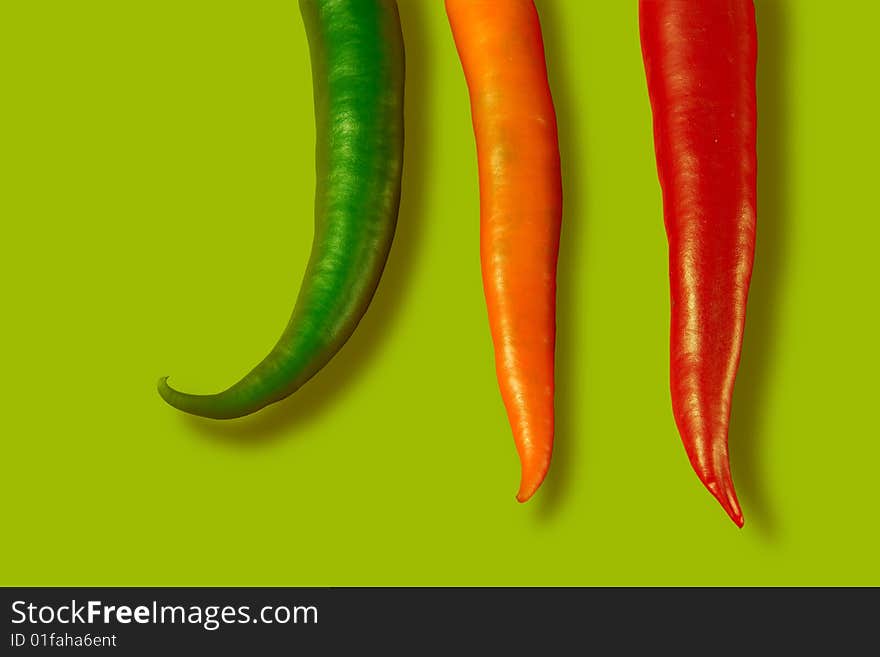 Green, orange and red chili peppers on green background