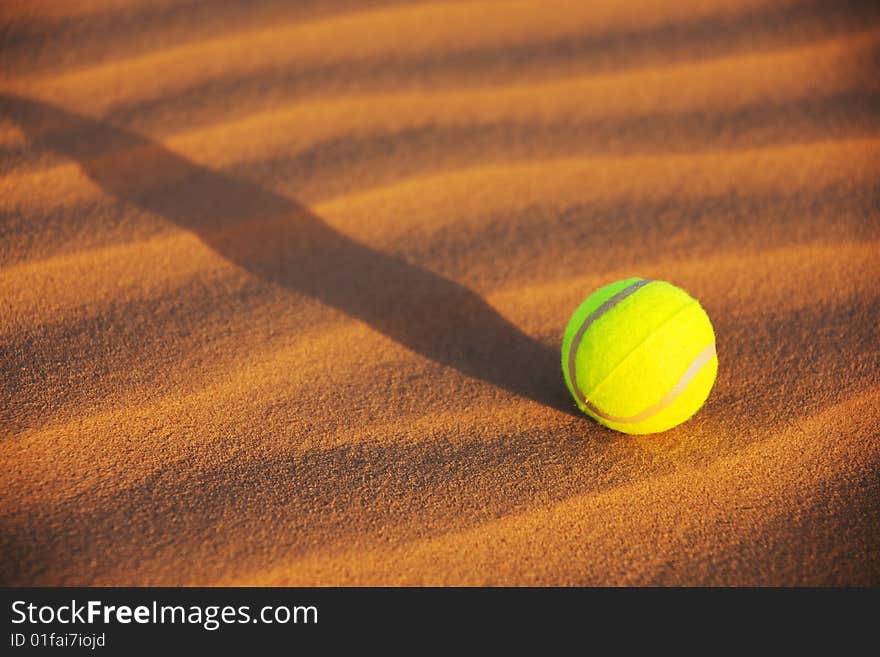 A yellow tennis ball in desert sand. A yellow tennis ball in desert sand