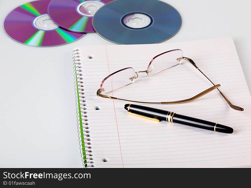 Notebook on white desk with glasses and cd-s. Notebook on white desk with glasses and cd-s.