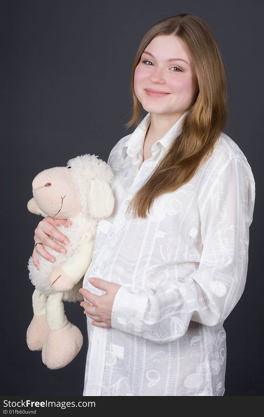 Beautiful pregnant woman in white holding toy on grey background. Beautiful pregnant woman in white holding toy on grey background