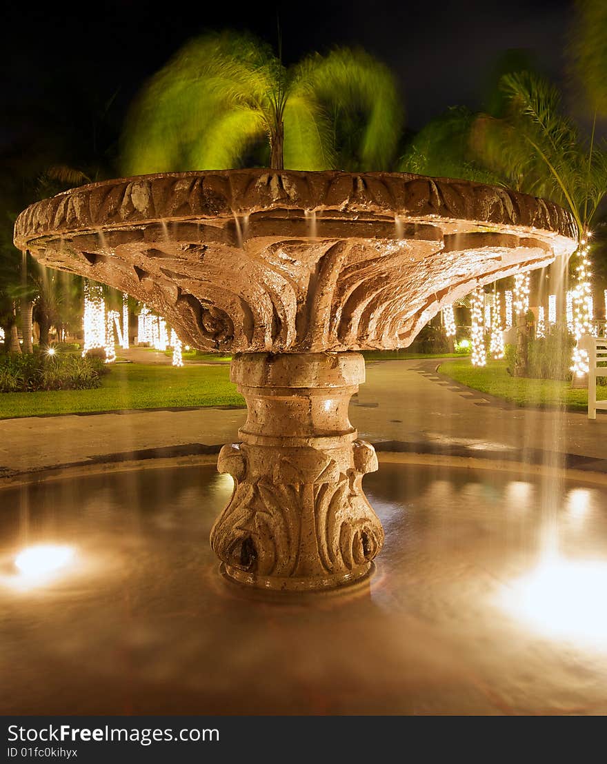 Water flowing from illuminated fountain at night in luxury resort, illuminated palm trees in background. Water flowing from illuminated fountain at night in luxury resort, illuminated palm trees in background