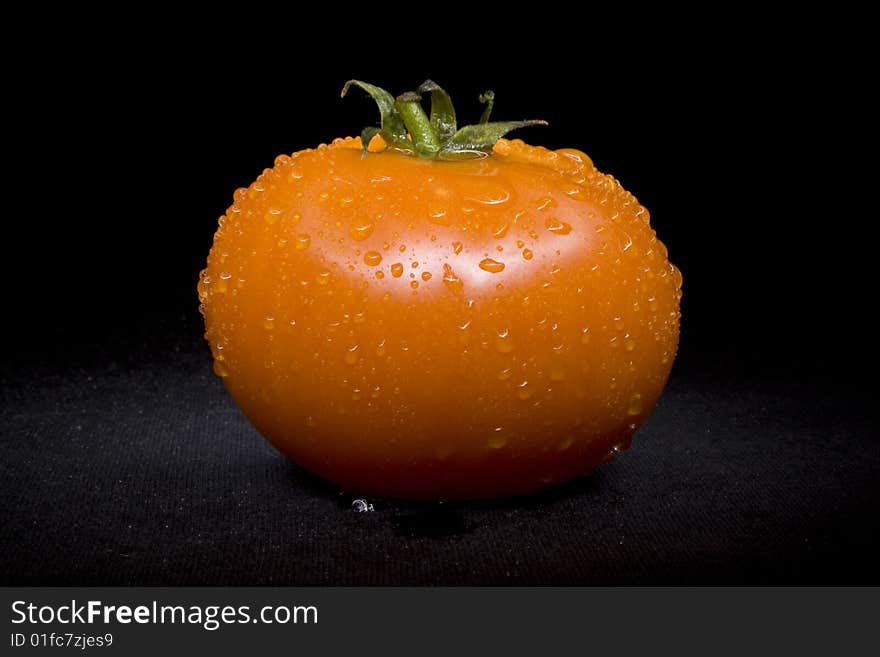 Tomato single with drops on black not isolated background