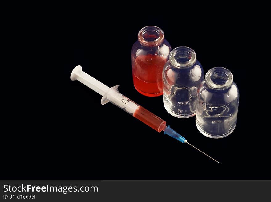 Three vials and a syringe with red medicine