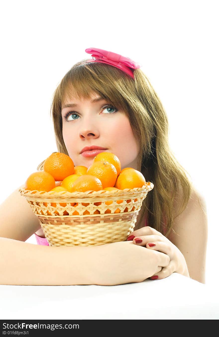 Beautiful dreamy young woman sitting by the table with a basket full of tangerines standing on it. Beautiful dreamy young woman sitting by the table with a basket full of tangerines standing on it