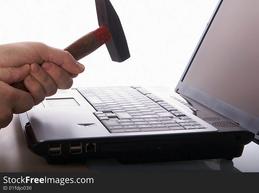 A hand hits a laptop with a hammer on a table. Isolated over white background. Copyspace also on the screen. A hand hits a laptop with a hammer on a table. Isolated over white background. Copyspace also on the screen.