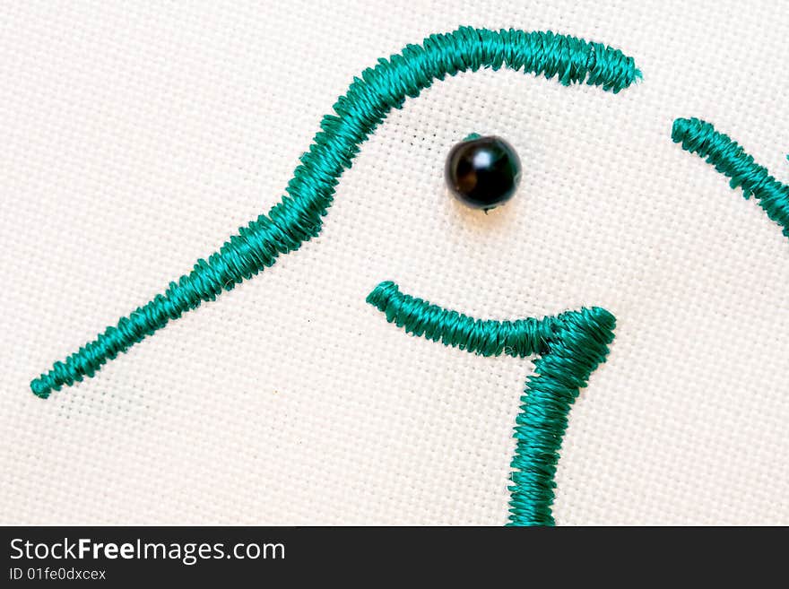 Closeup of embroidered bird head  green yarn  black button eye on white fabric