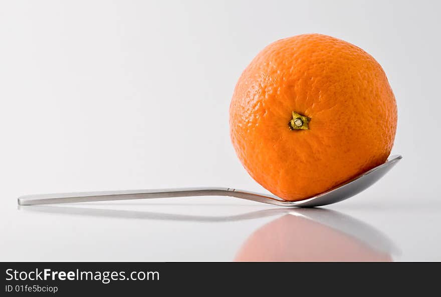 Metal tea-spoon with tangerine in it, reflective surface and shadows