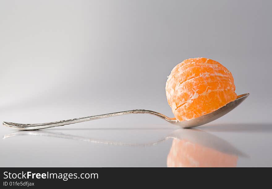 Metal teaspoon with a segment of tanregine in it, reflective surface, shadows