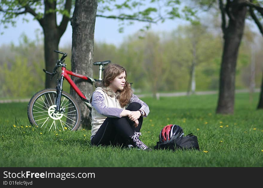 Young girl siting on a grass after a bike ride. bicycle is on the background. Young girl siting on a grass after a bike ride. bicycle is on the background