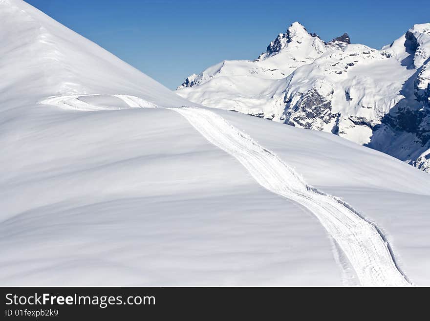 A track up a mountain ridge with a range of mountains in the background