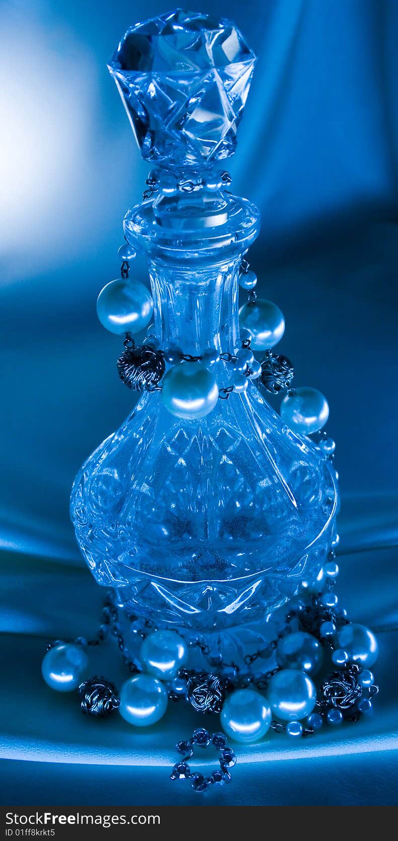 A small bottle from glass twined about beads from pearls on a dark blue background. A small bottle from glass twined about beads from pearls on a dark blue background