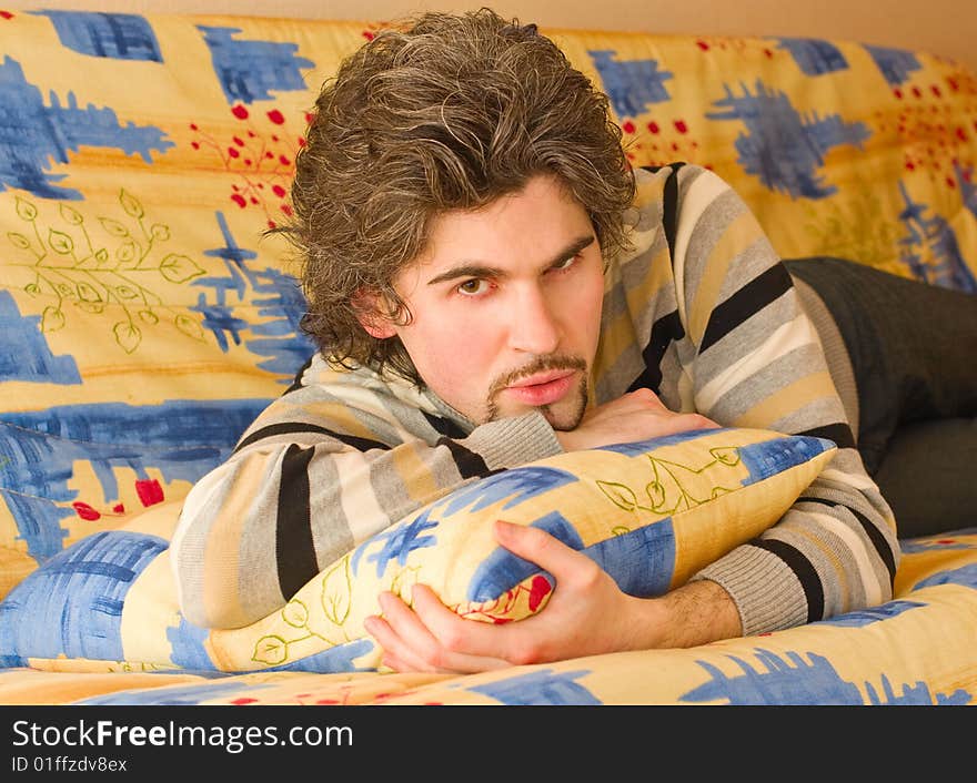 Young serious dark haired caucasian man in striped sweater lying on country style sofa. Young serious dark haired caucasian man in striped sweater lying on country style sofa