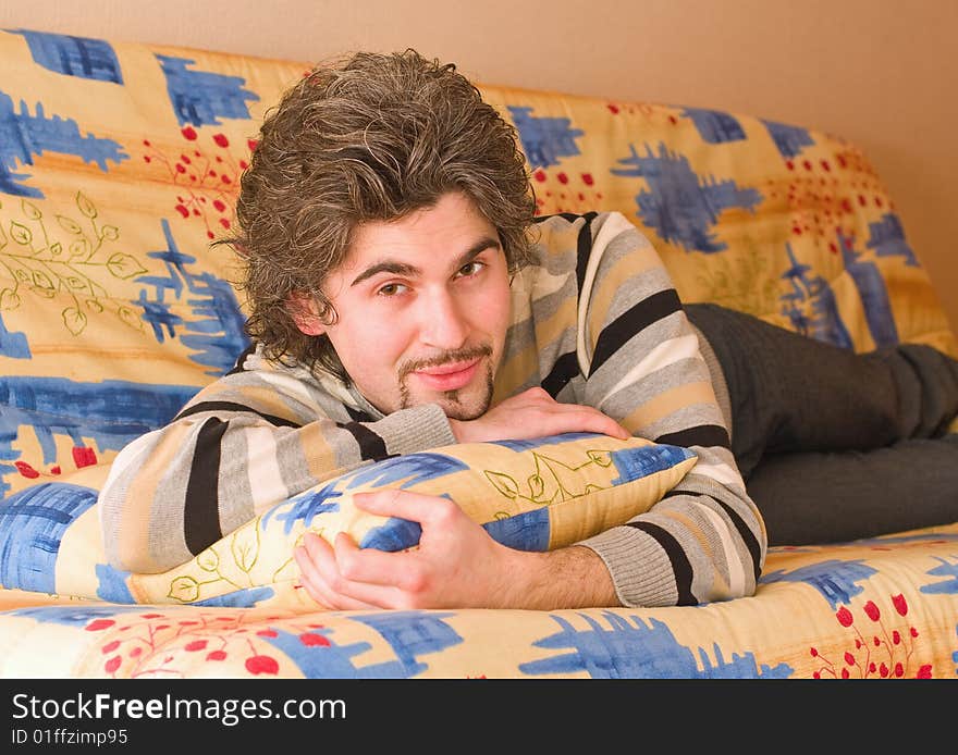 Young smiley dark haired caucasian man in striped sweater lying on country style sofa. Young smiley dark haired caucasian man in striped sweater lying on country style sofa