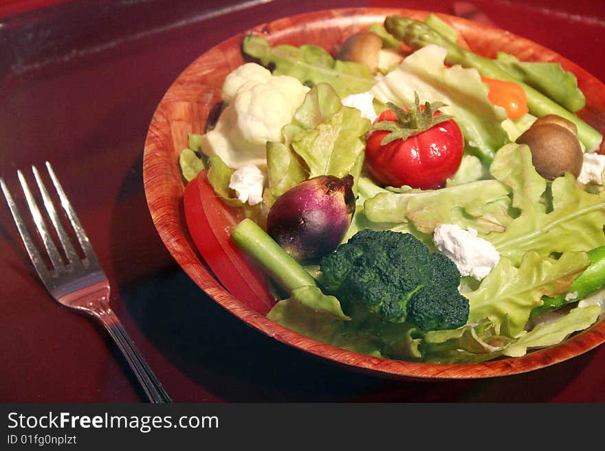 A fresh salad is full of vegetables with a fork nearby.