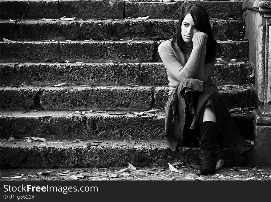 Young thoughtful woman sitting in stone stairs.