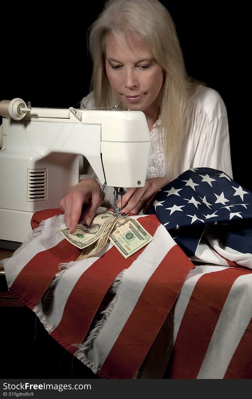 Attractive blond woman sewing American currency into the mending of a tattered American flag on a sewing machine. Attractive blond woman sewing American currency into the mending of a tattered American flag on a sewing machine.