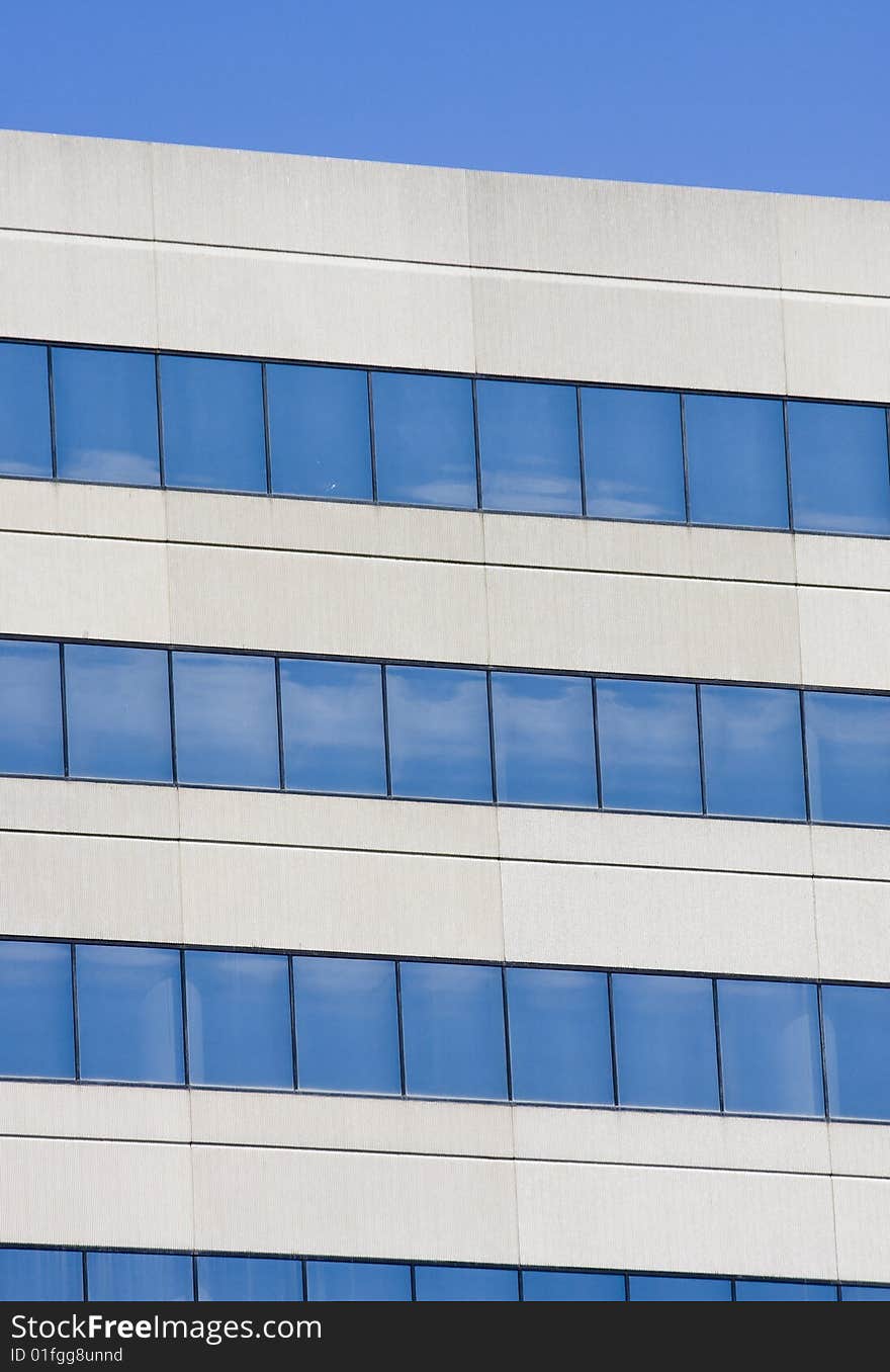 Details of a grey concrete building with blue windows reflecting sky. Details of a grey concrete building with blue windows reflecting sky