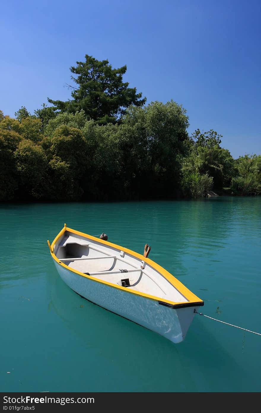 A clean white boat floating on a deep green river, trees and blue sky in background