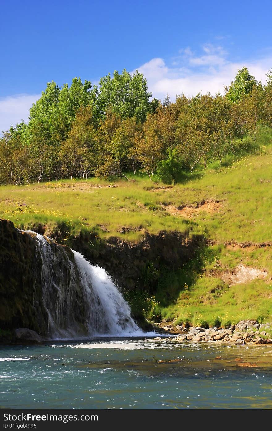 A small waterfall during summer, set against gentle hills with small trees on top of it. A small waterfall during summer, set against gentle hills with small trees on top of it