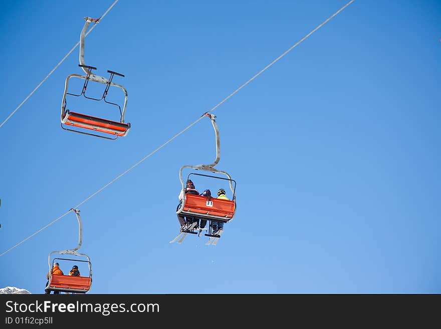 Skiers are riding in chairlift in a ski area, low angle view, Italy. Large copy-space at the top.