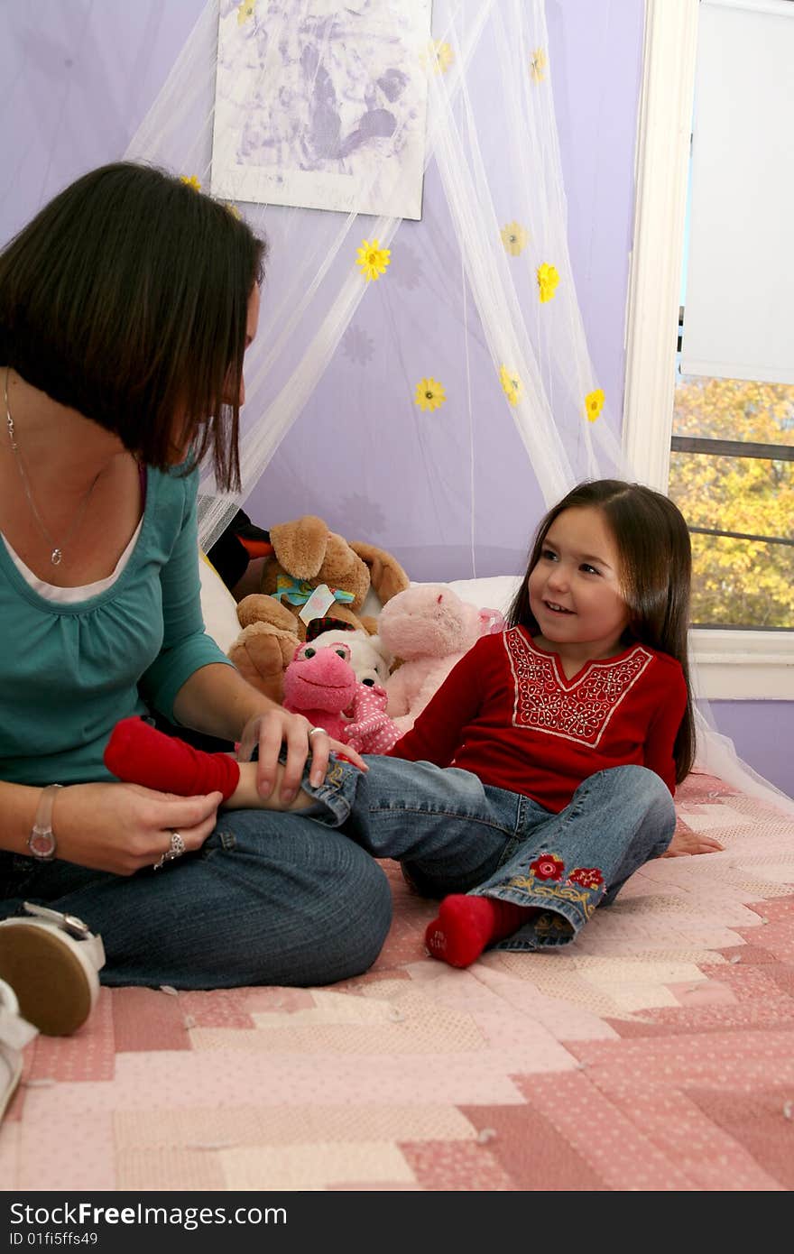 Mother removing her little girl's sock and sitting on the bed. Mother removing her little girl's sock and sitting on the bed