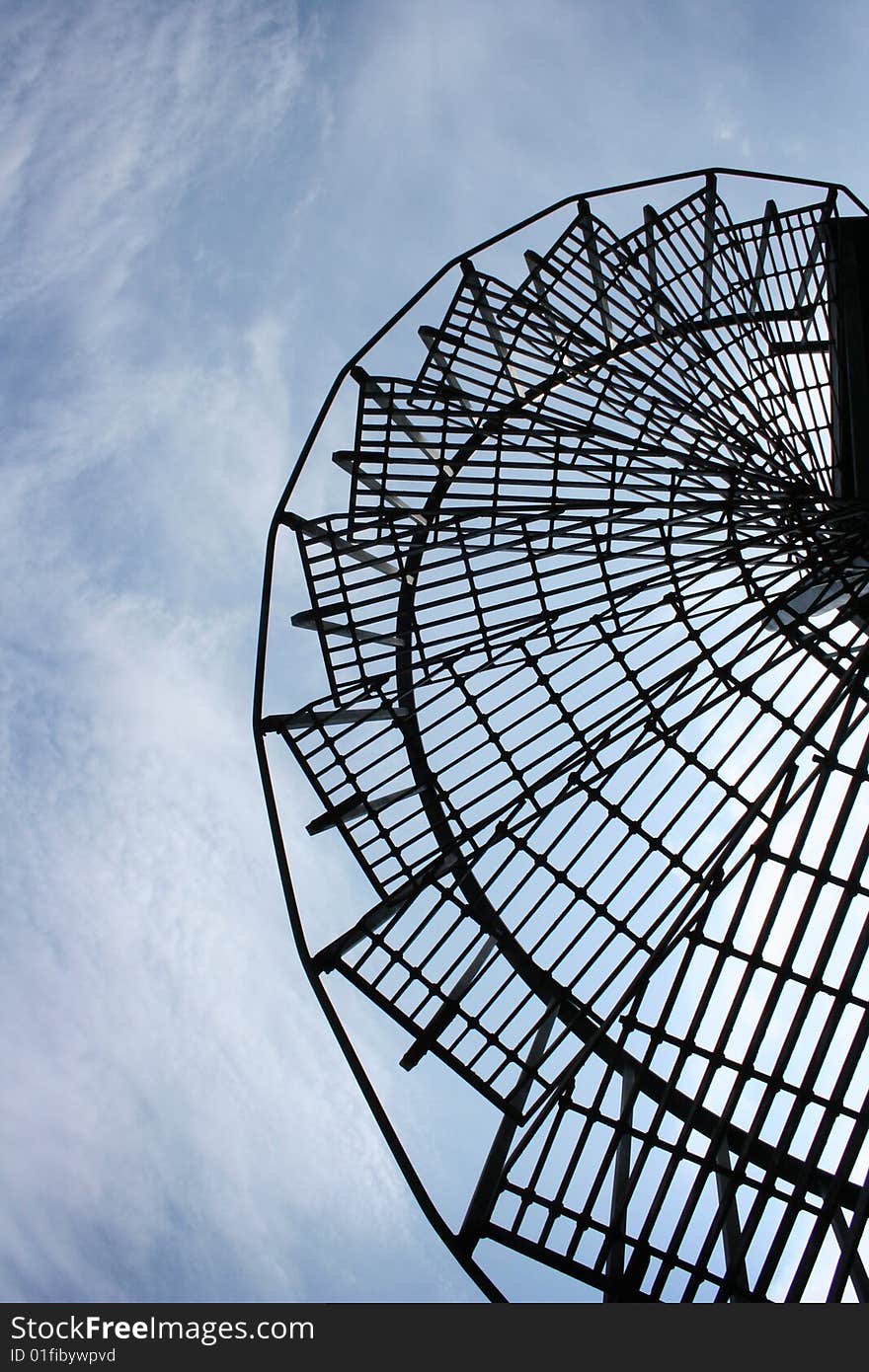 A metal winding staircase against a blue sky.