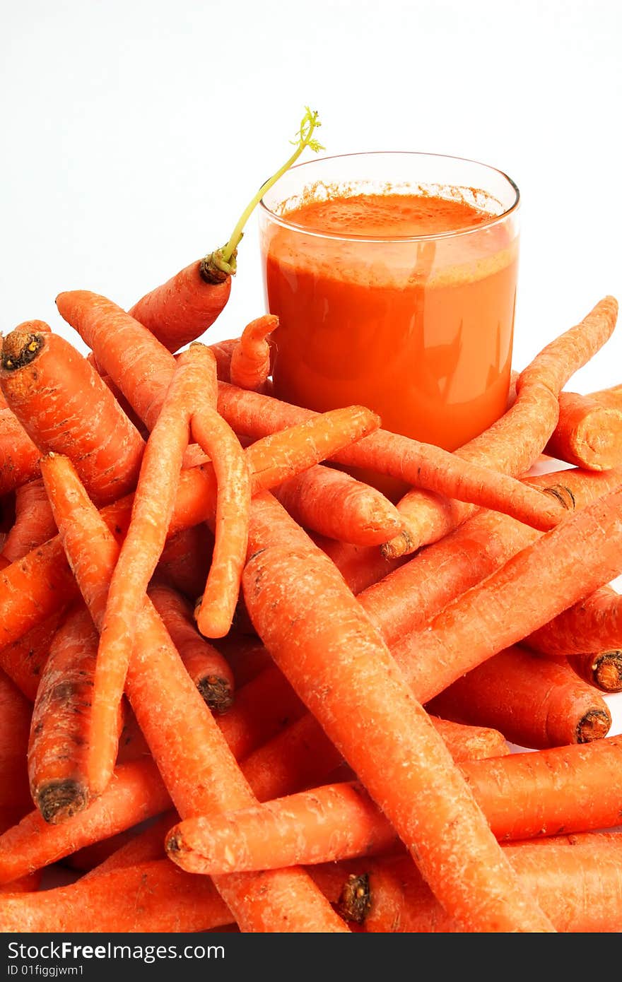 A glass of fresh carrot juice and a bunch of carrots in foreground. A glass of fresh carrot juice and a bunch of carrots in foreground.