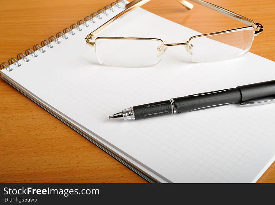 Notebook, glasses and pen on table