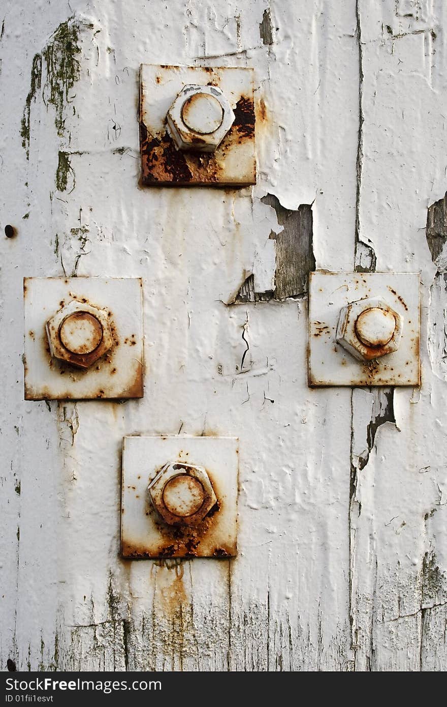 Four rusty bolts on an old wooden fencepost. Bolts are not placed symmetrically. Paint is peeling off.