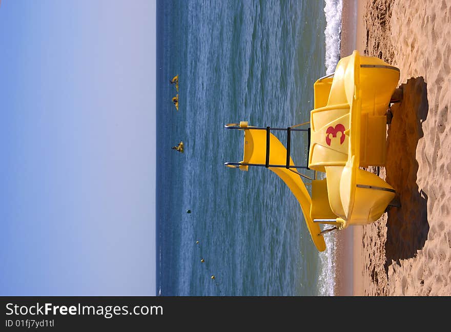 Yellow pedalboat on a sandy beach with the ocean in the background. Yellow pedalboat on a sandy beach with the ocean in the background