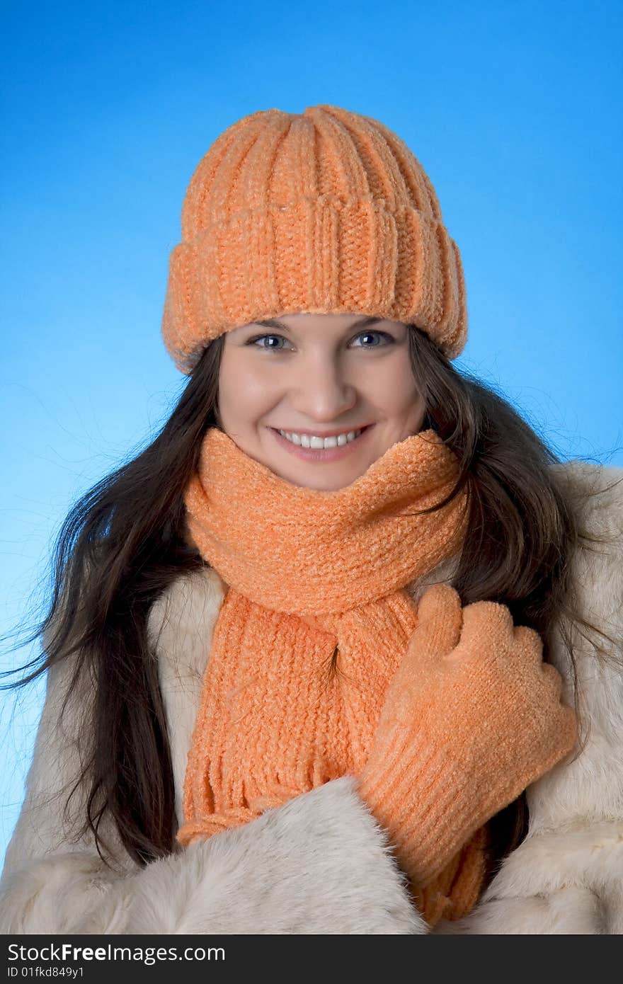 Picture of a beautiful brunette girl in the orange cap and coat on a blue background