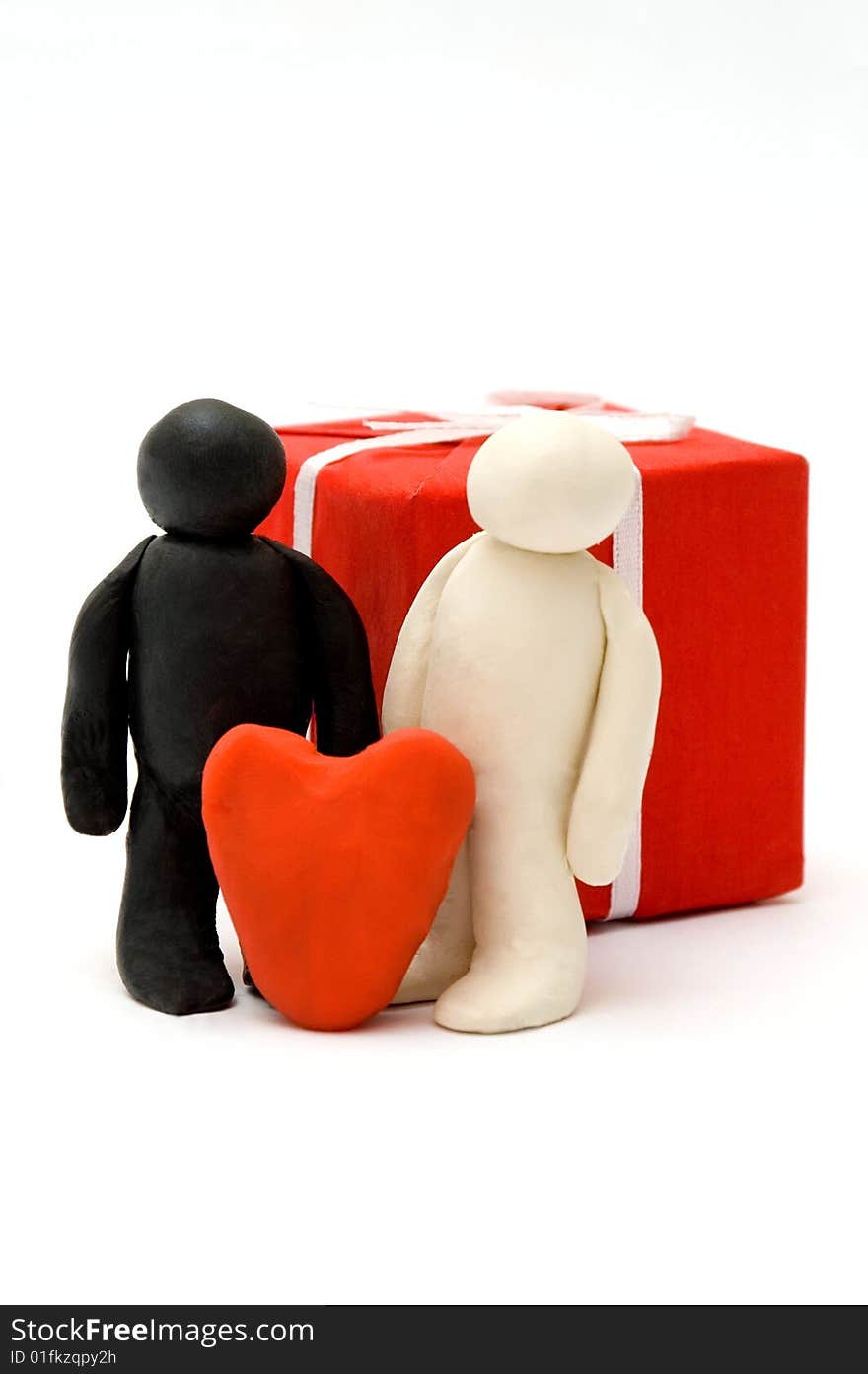 Two Plasticine persons against a box with a gift and with heart