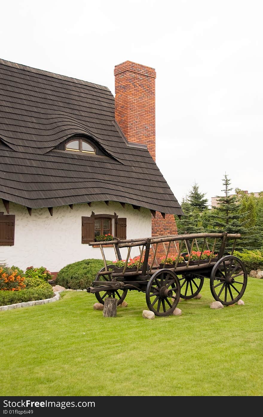 Cottage with thatched roof, old fashioned wooden carriage in foreground garden, Poland.