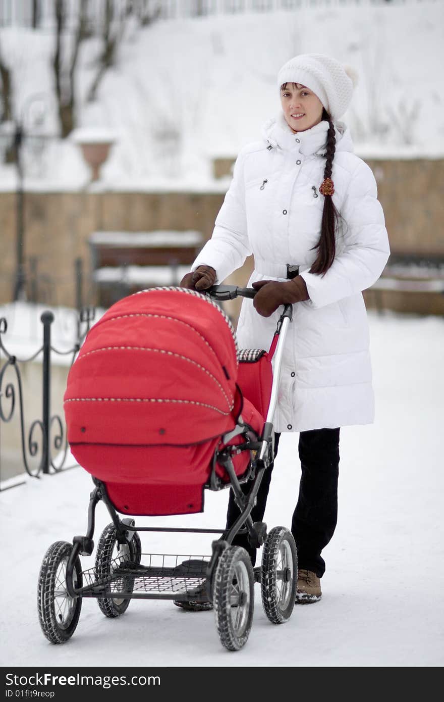 Woman in white jacket with red baby carriage outdoors - shallow DOF. Woman in white jacket with red baby carriage outdoors - shallow DOF