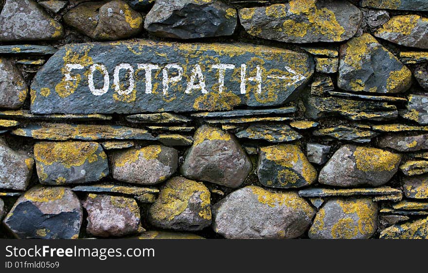 Footpath sign on stone wall with yellow lichen