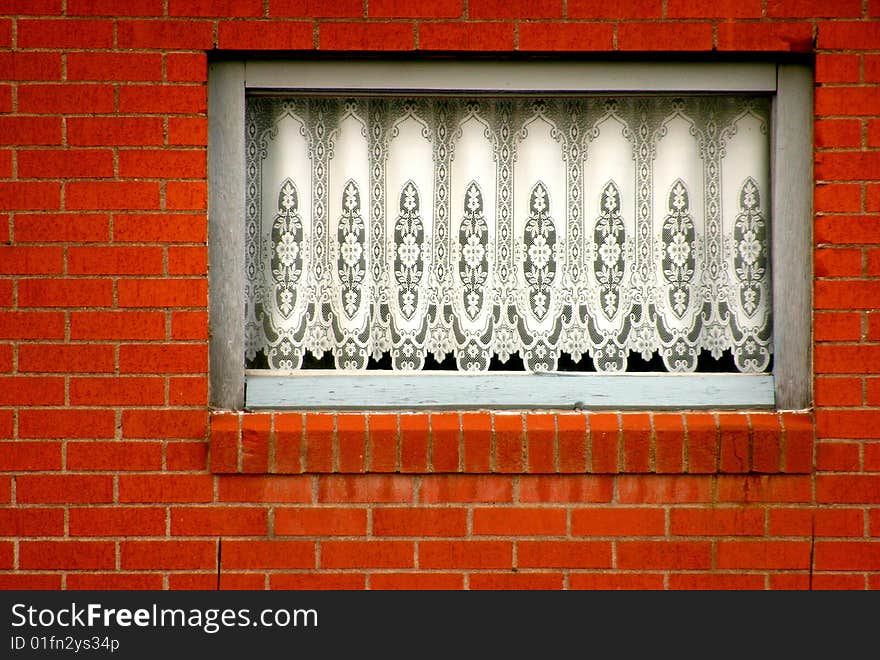 White lace drapery in a window in a brick wall. White lace drapery in a window in a brick wall.