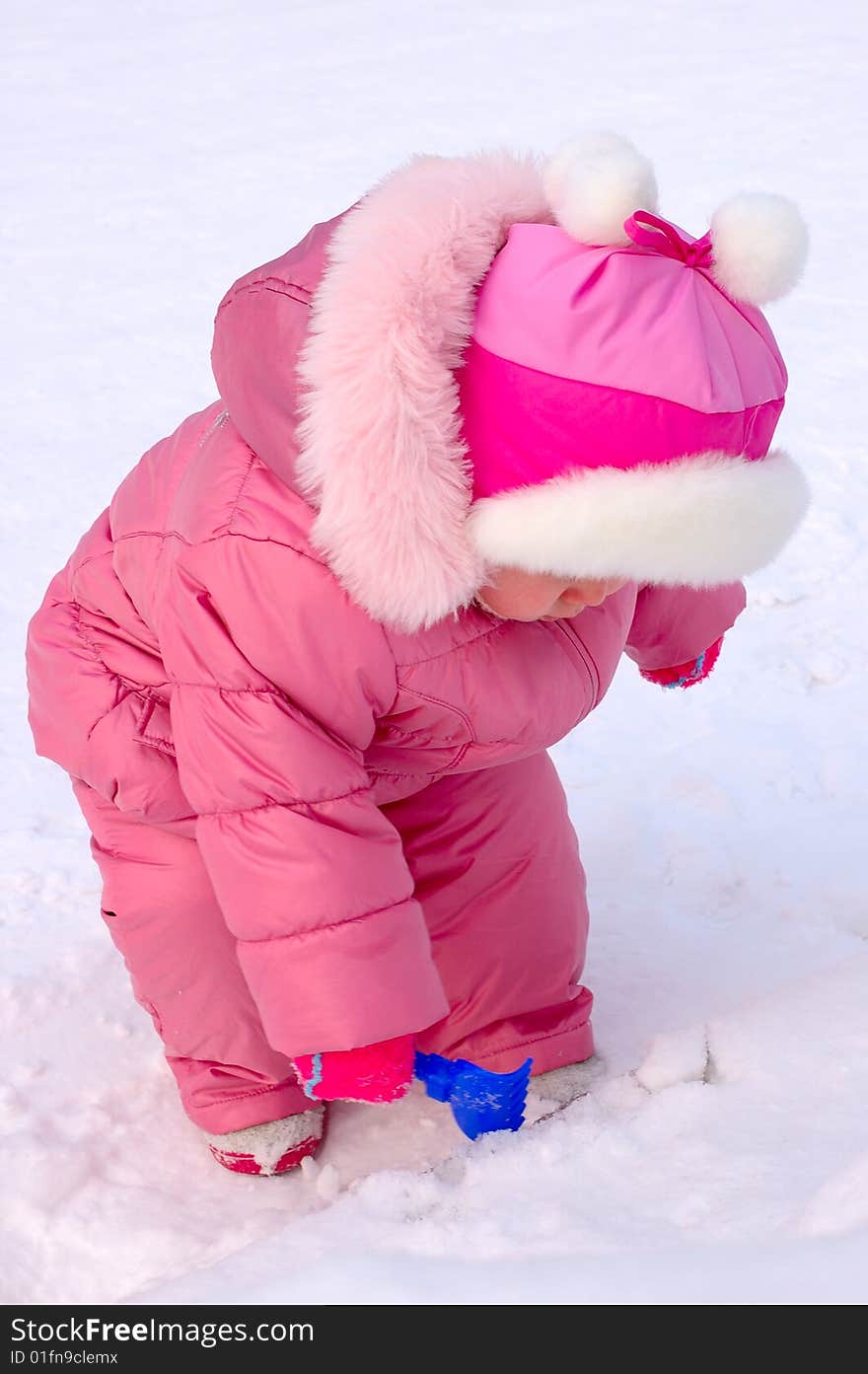 Pretty little girl with blue plastic toy rake in winter outerwear stay on snow-covered ground. Pretty little girl with blue plastic toy rake in winter outerwear stay on snow-covered ground.